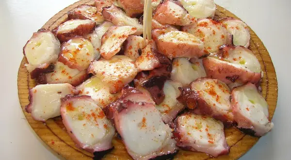 A delicious serving of pulpo a feira, tender octopus seasoned with paprika and olive oil, artfully arranged on a wooden platter.