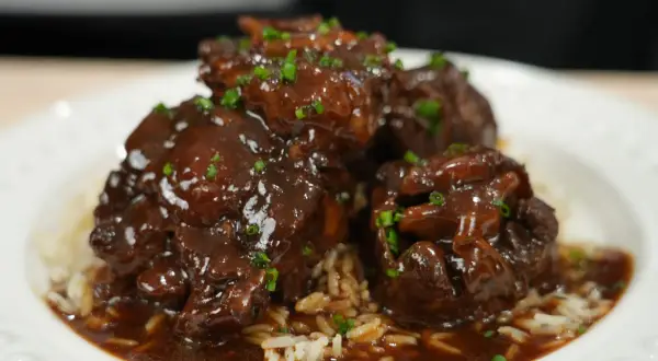 Tender, braised oxtail pieces in a rich, dark sauce, served over fluffy white rice and garnished with chopped green onions. A delicious oxtail recipe.