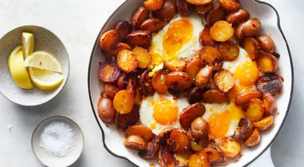 Huevos rotos: a hearty skillet dish with fried eggs nestled among crispy, golden-brown potato slices, served with lemon wedges and sea salt.