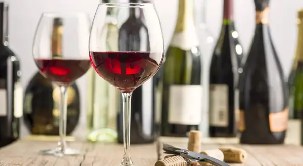 Two glasses of red wine, bottles, and corks on a wooden table. Imagine the rich, fruity mencia geschmack.
