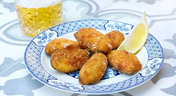 Crispy fried tiger mussels served on a blue and white plate with a lemon wedge and a glass of beer.