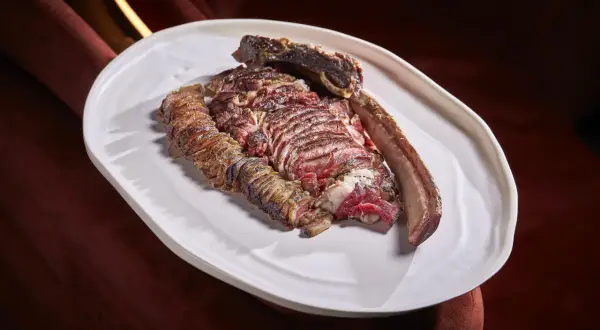 A perfectly cooked chuleton, a thick-cut bone-in steak, rests on a white platter, showcasing its juicy, red interior and seared crust.