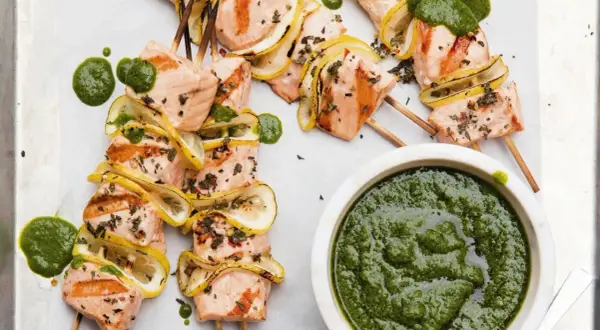 Grilled salmon skewers with lemon slices and a vibrant green sauce, ready to be dipped.