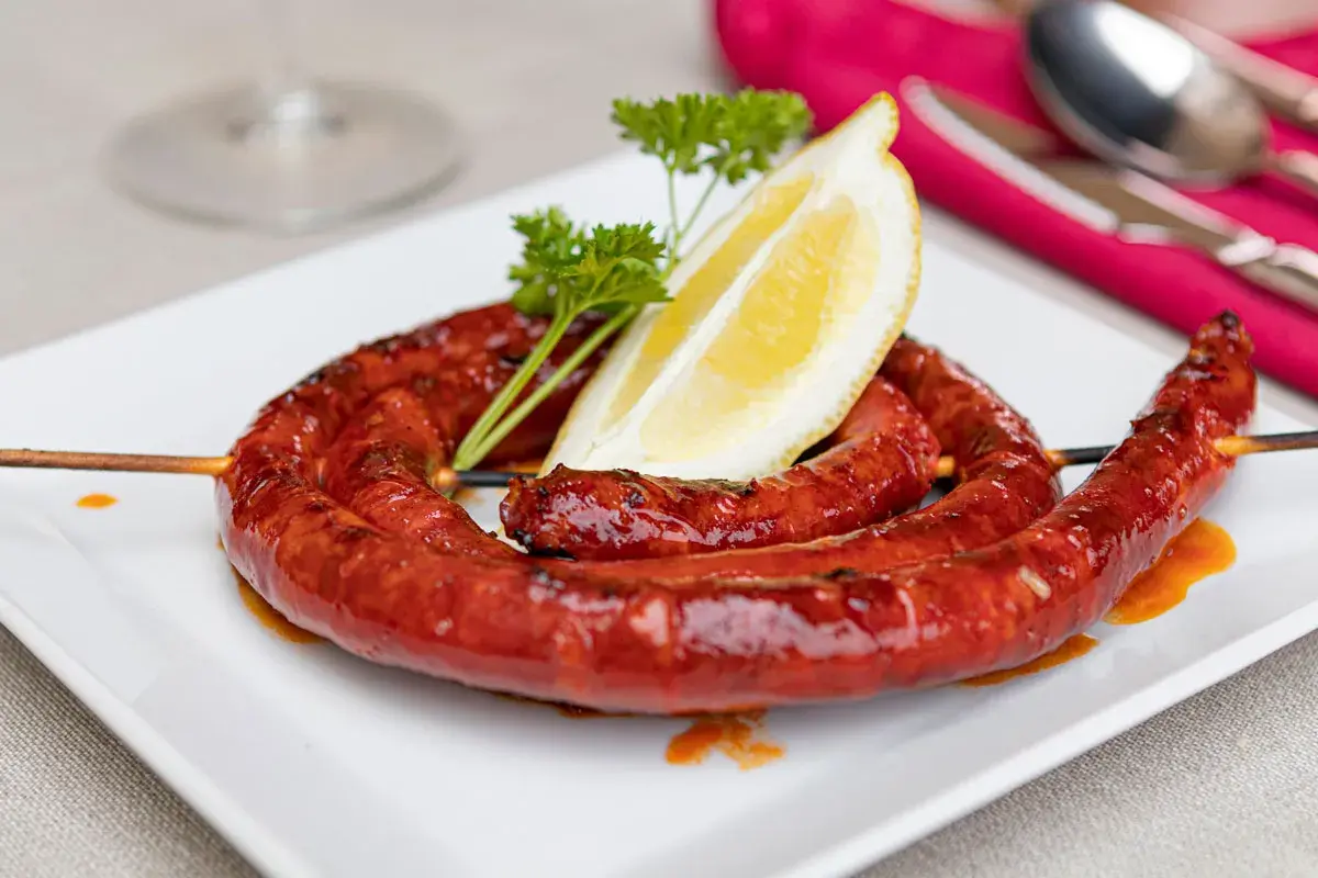 A coiled chistorra sausage, grilled to perfection, served on a white plate with a lemon wedge and parsley. A delicious chistorra recipe.