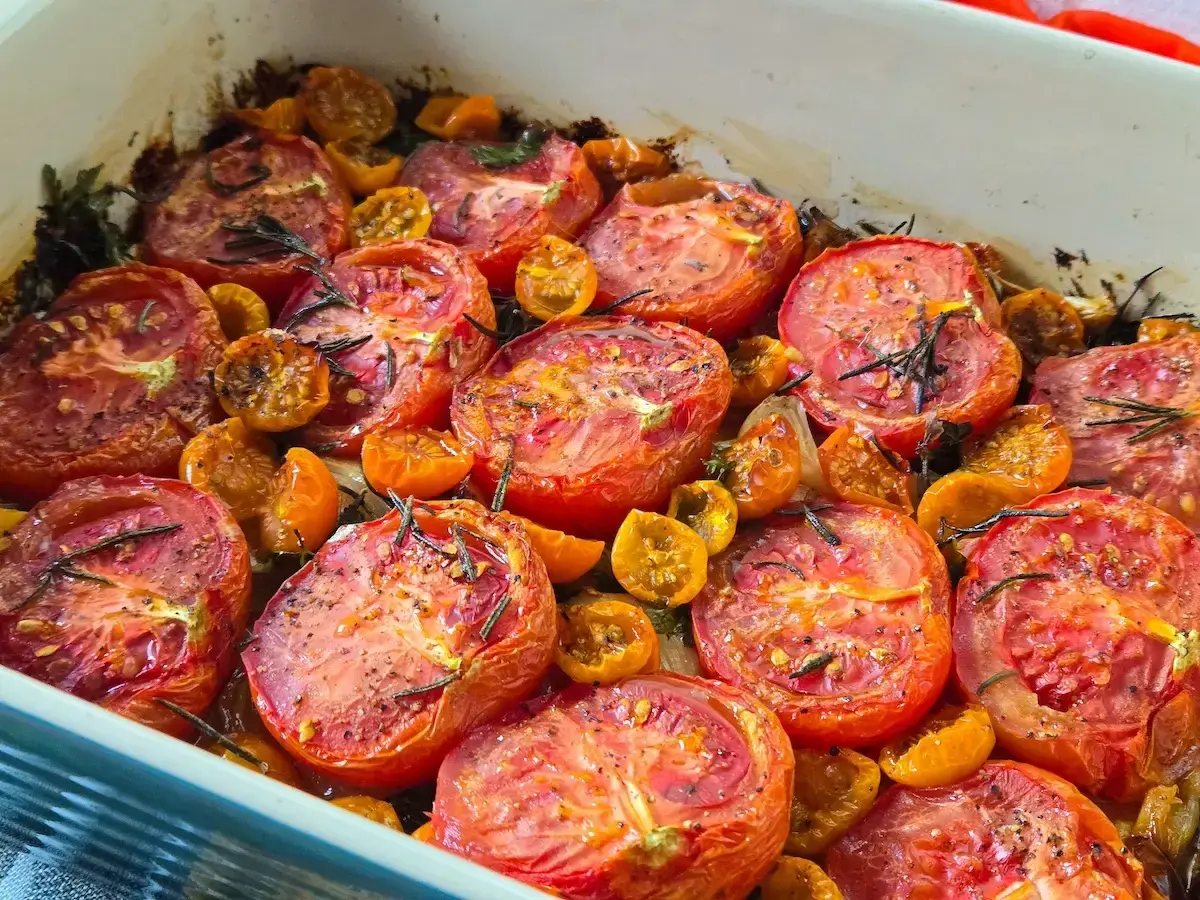 A baking dish filled with juicy, slow roasted tomatoes and cherry tomatoes, seasoned with herbs and spices.