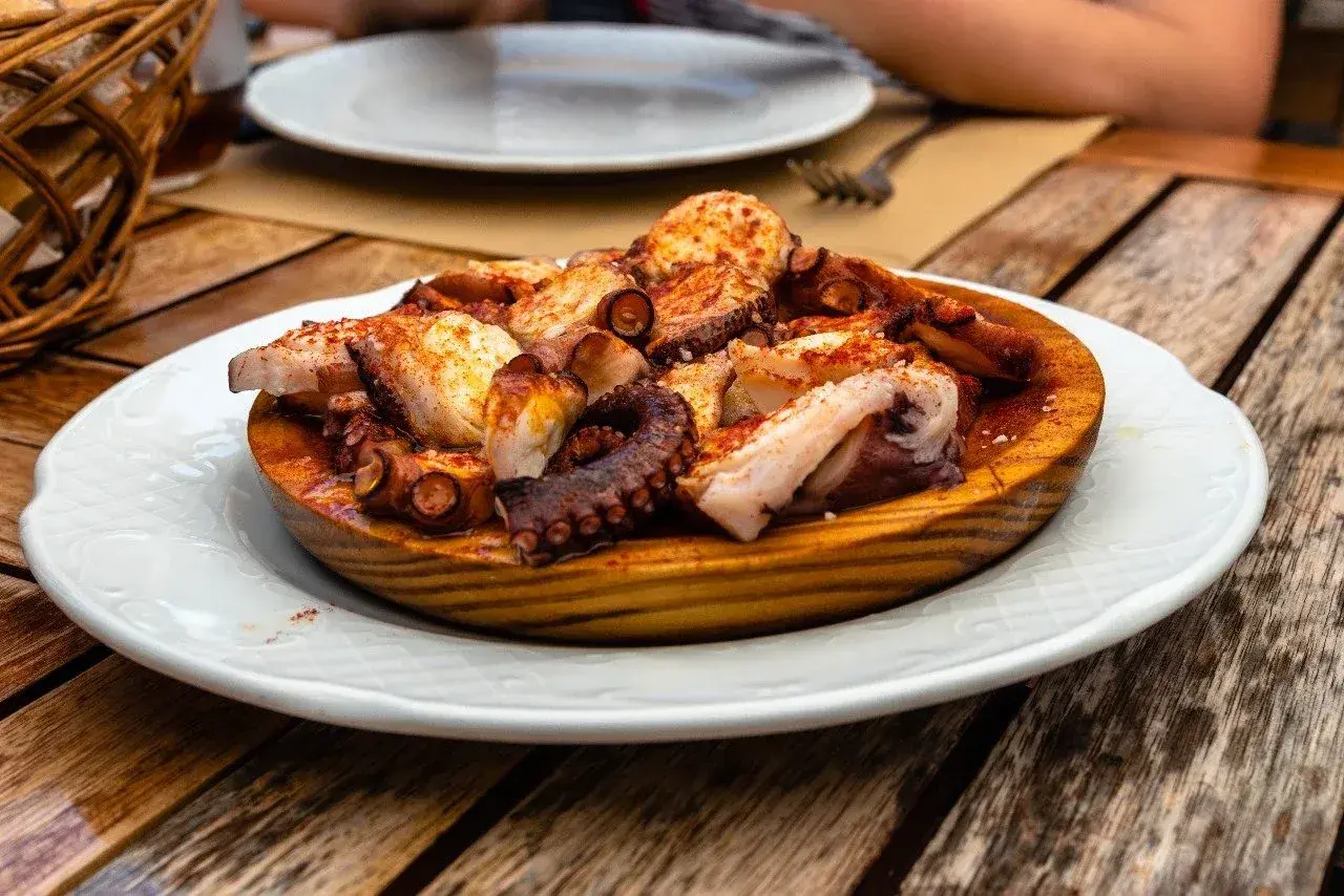 A delicious Spanish octopus dish, seasoned with paprika and served on a wooden platter on a rustic table.