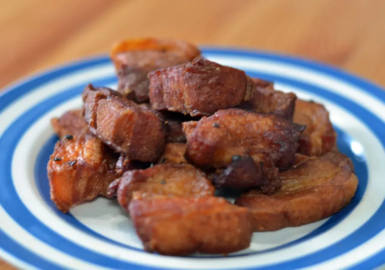 A pile of crispy fried pork belly, or chicharrones, on a blue and white striped plate.