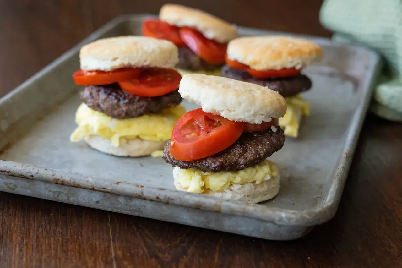 Fluffy biscuits layered with scrambled eggs, a savory goose sausage patty, and fresh tomato slices.