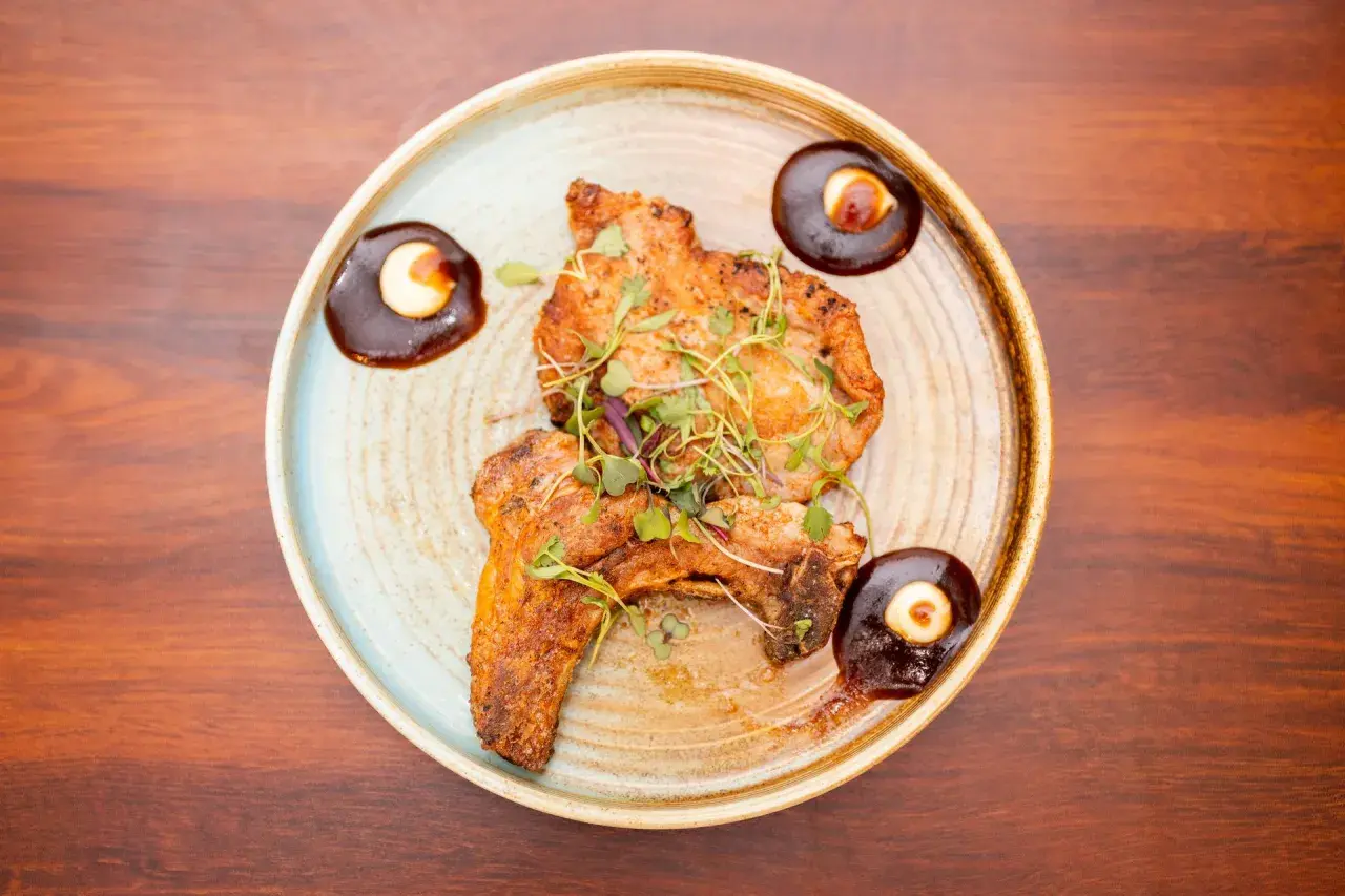 Two pieces of grilled steak, garnished with microgreens, are served as steak tapas with a rich sauce and a dollop of cream.