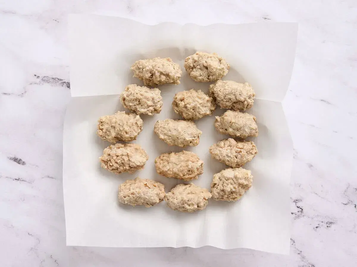 A dozen uncooked croquetas de pollo are arranged on white parchment paper, ready for frying.
