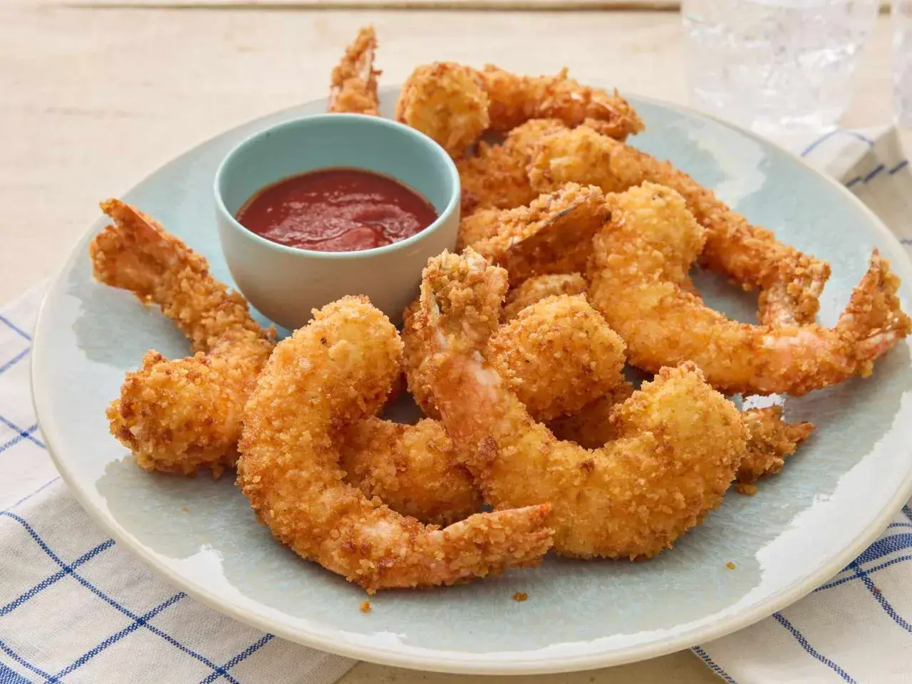 Crispy fried shrimp piled high on a plate, with a small bowl of red dipping sauce.