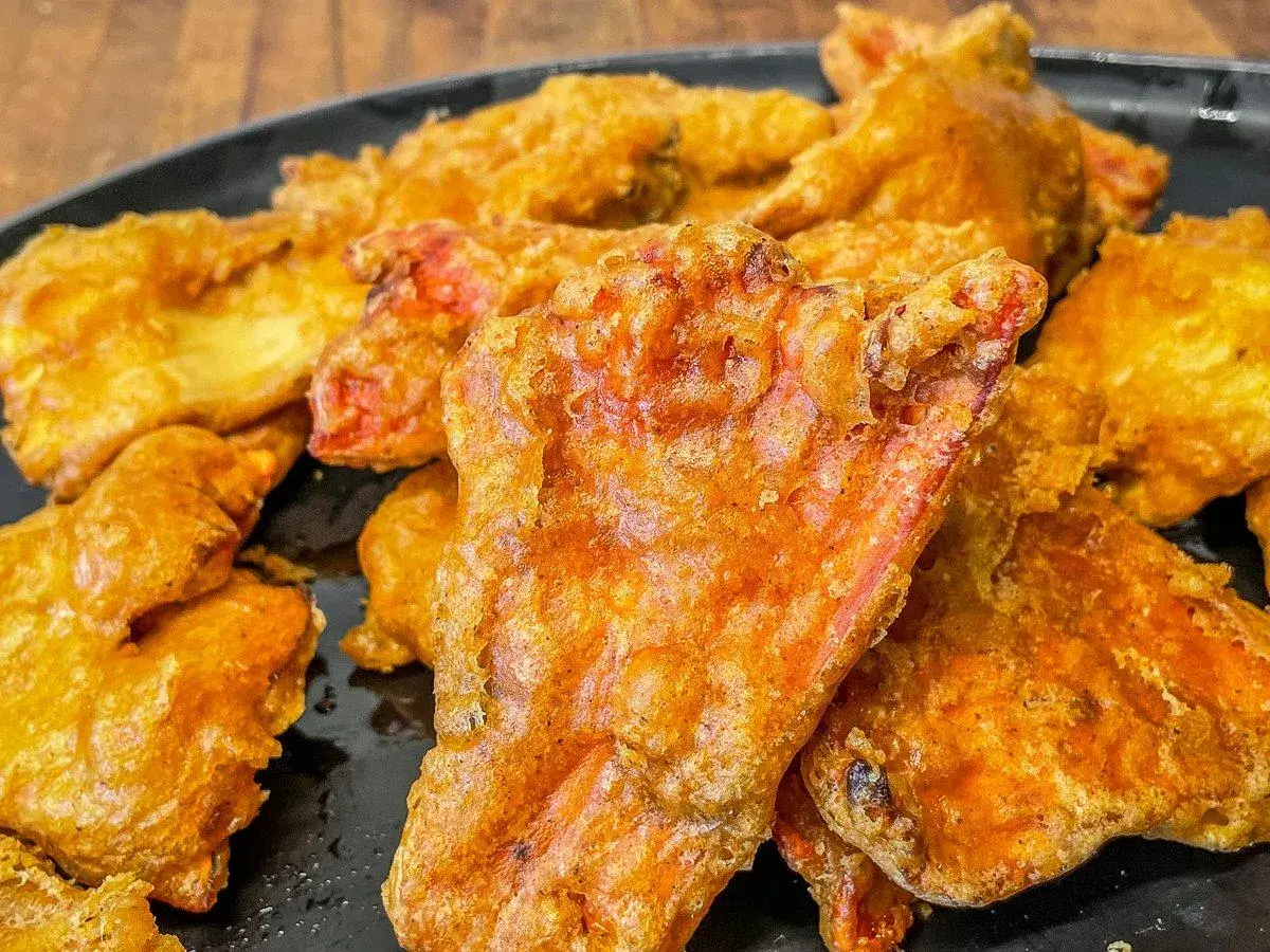 Crispy, golden-fried pieces, possibly part of a delicious chicken of the woods recipe, piled on a black plate.