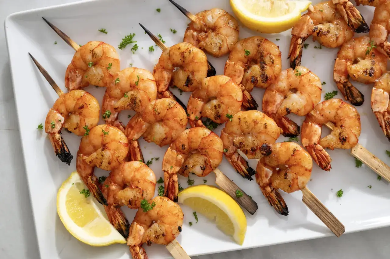 A platter of perfectly grilled shrimp skewers, seasoned and garnished with fresh parsley and lemon wedges.