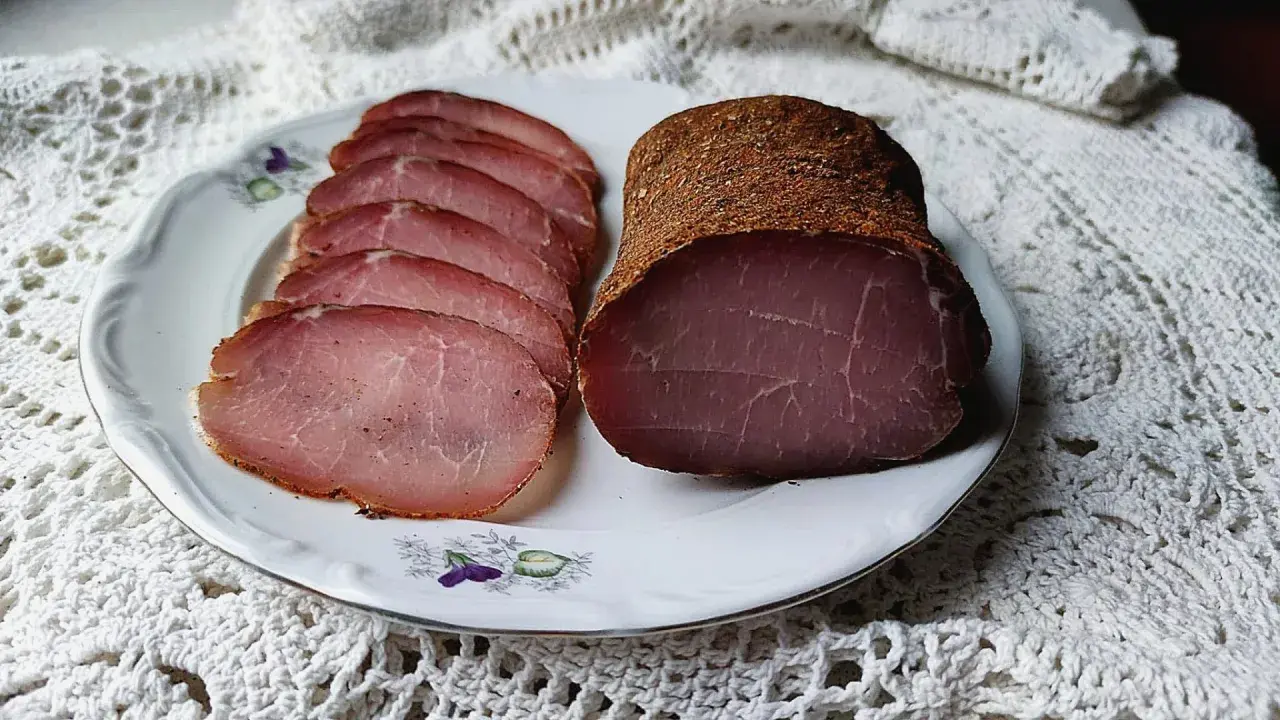 A whole and sliced cured pork loin, seasoned with spices, rests on a decorative plate.
