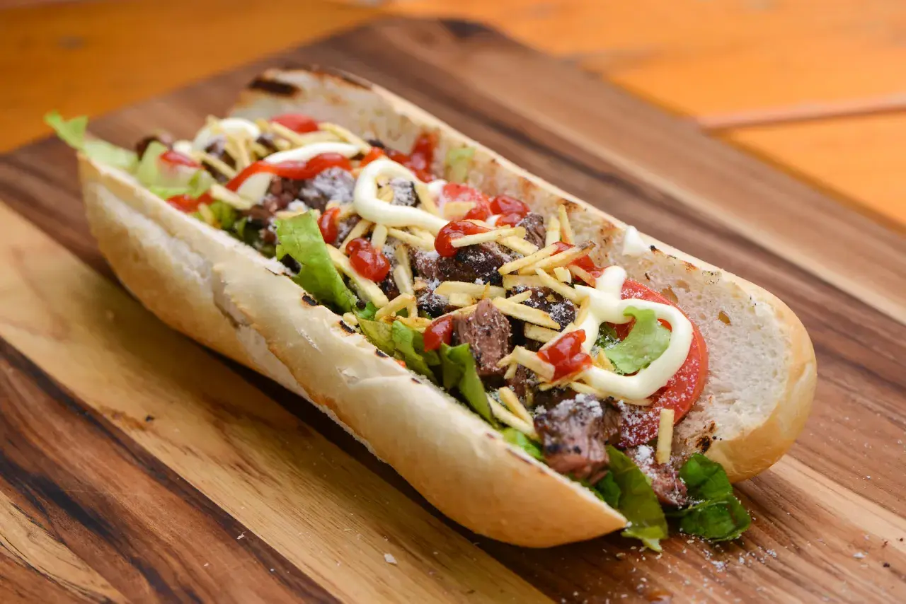 A delicious pepito sandwich overflowing with tender steak, crisp lettuce, tomato, shoestring fries, and drizzled with ketchup and mayonnaise.