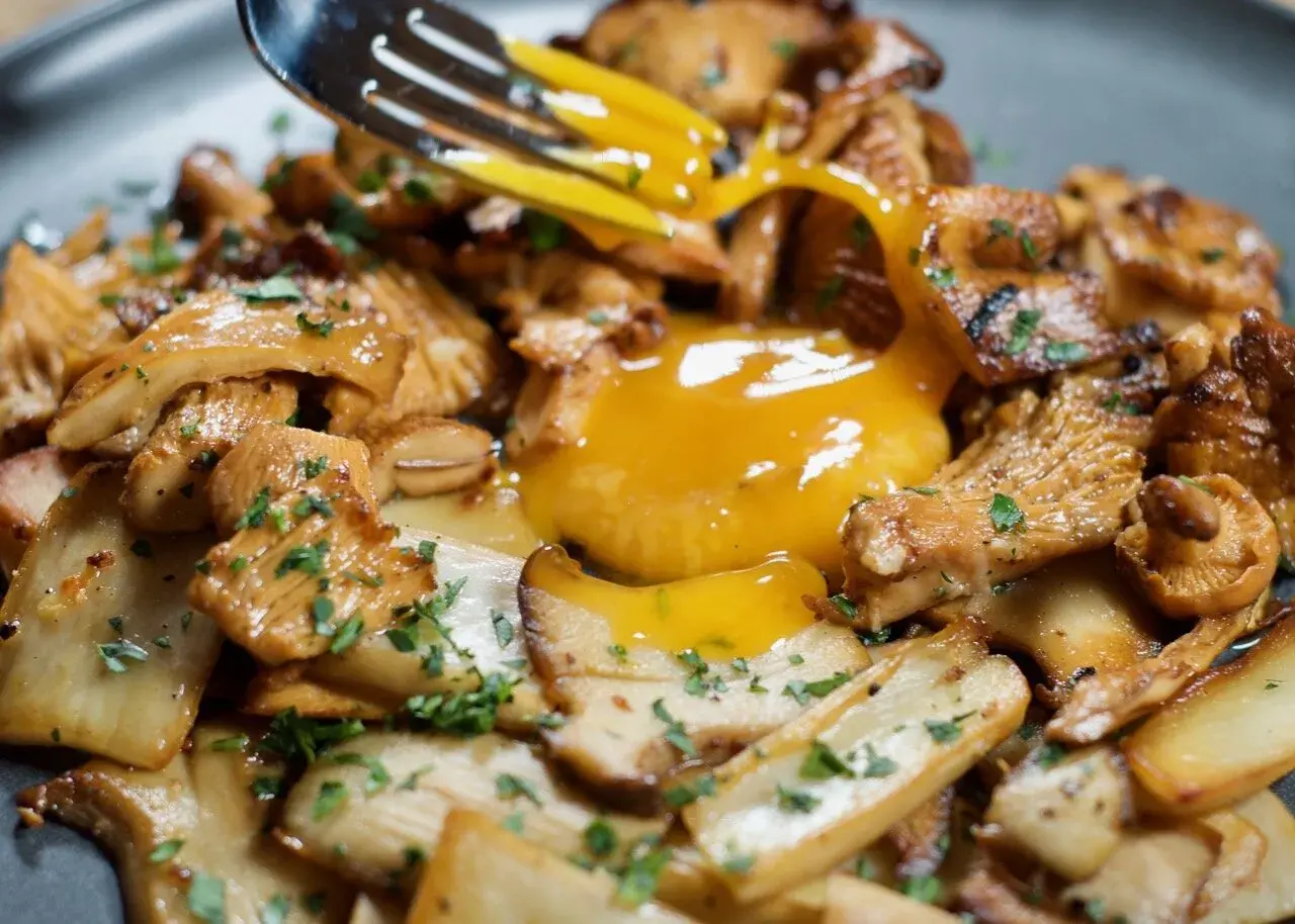 A fork breaks a rich egg yolk over a bed of perfectly grilled mushroom recipe, garnished with fresh parsley.