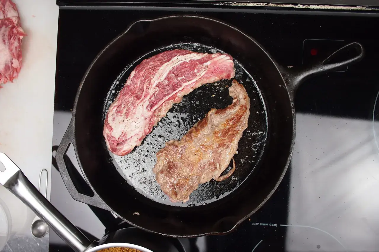 A pluma steak, a prized cut from the pork loin, sizzles in a cast-iron skillet. One side is perfectly seared, the other still raw and marbled.