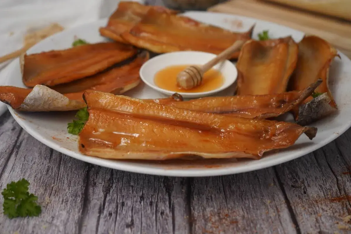 A plate of glistening smoked trout fillets, with a small dish of honey and a honey dipper. A delicious start to any meal.
