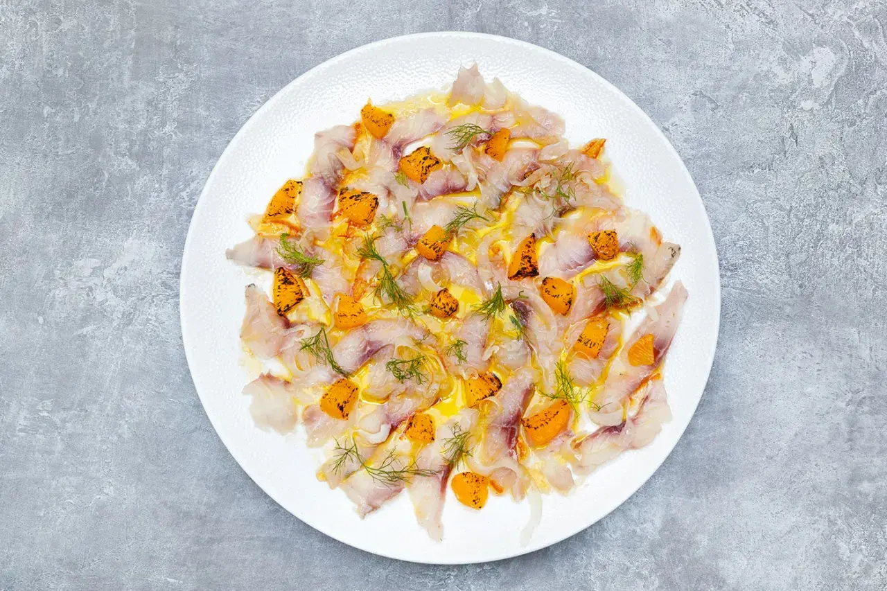 Thinly sliced sea bass crudo, glistening with olive oil and dotted with bright orange citrus segments and fresh dill.