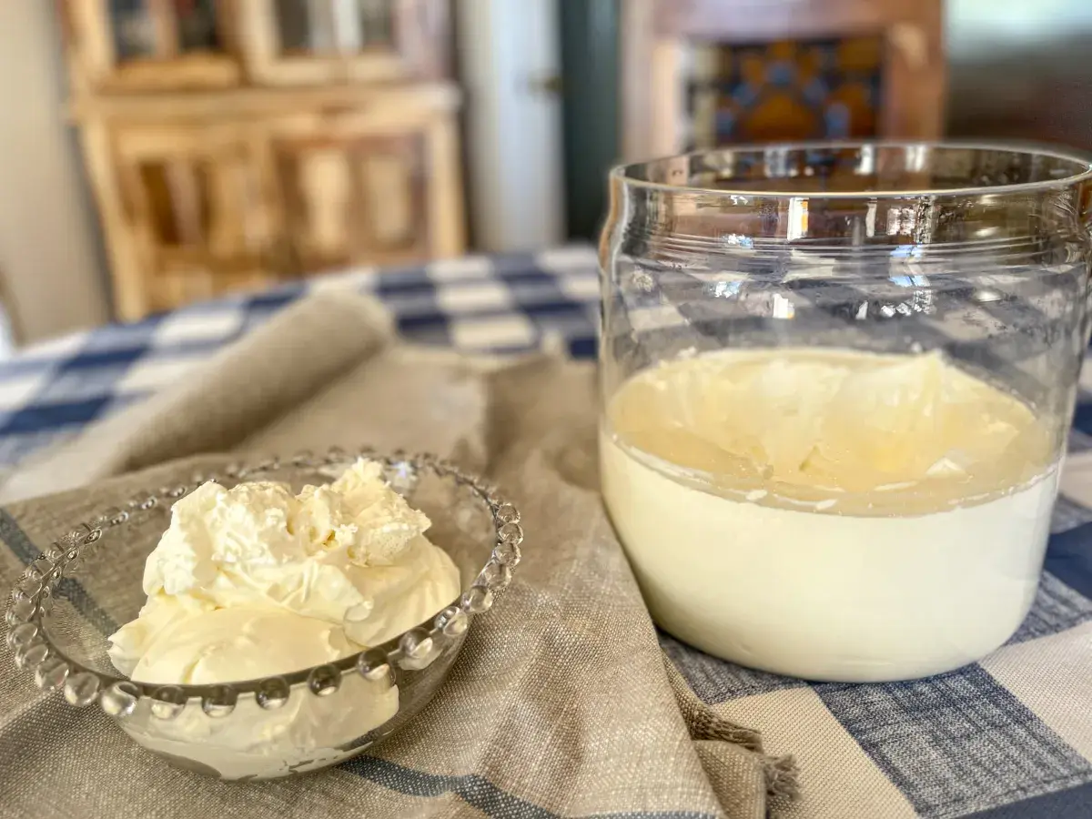A small glass bowl overflows with fluffy crème fraîche, next to a jar of the creamy dairy product.