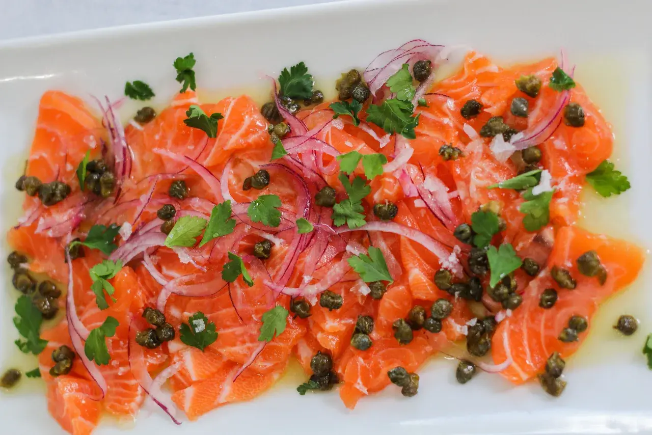Thinly sliced salmon crudo, dressed with olive oil, capers, red onion, and parsley, is a refreshing appetizer.