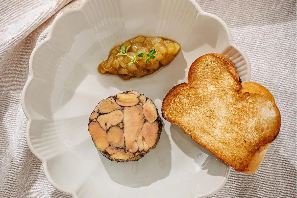 A slice of duck terrine with a dollop of compote and heart-shaped toast on a scalloped plate.