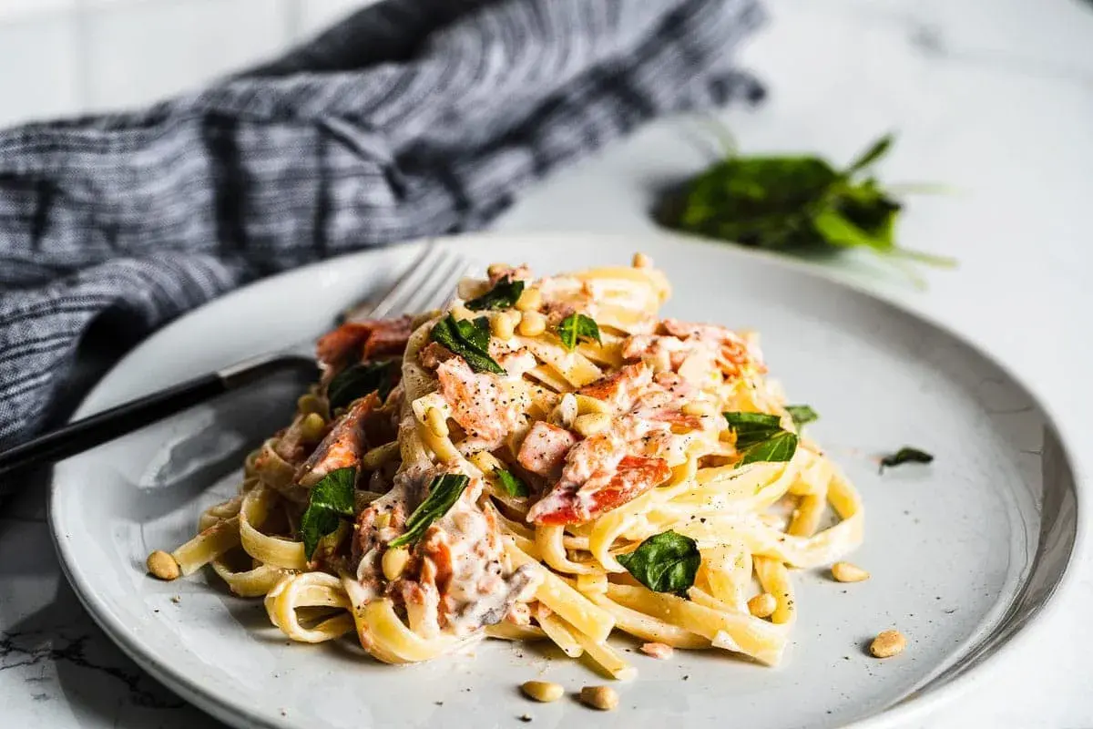 A plate of creamy smoked salmon pasta, garnished with fresh basil and pine nuts.