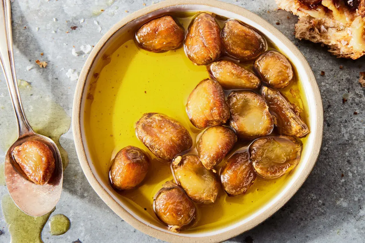 Golden garlic cloves swimming in olive oil, a delicious result of how to make garlic confit. A spoon holds one tender clove.