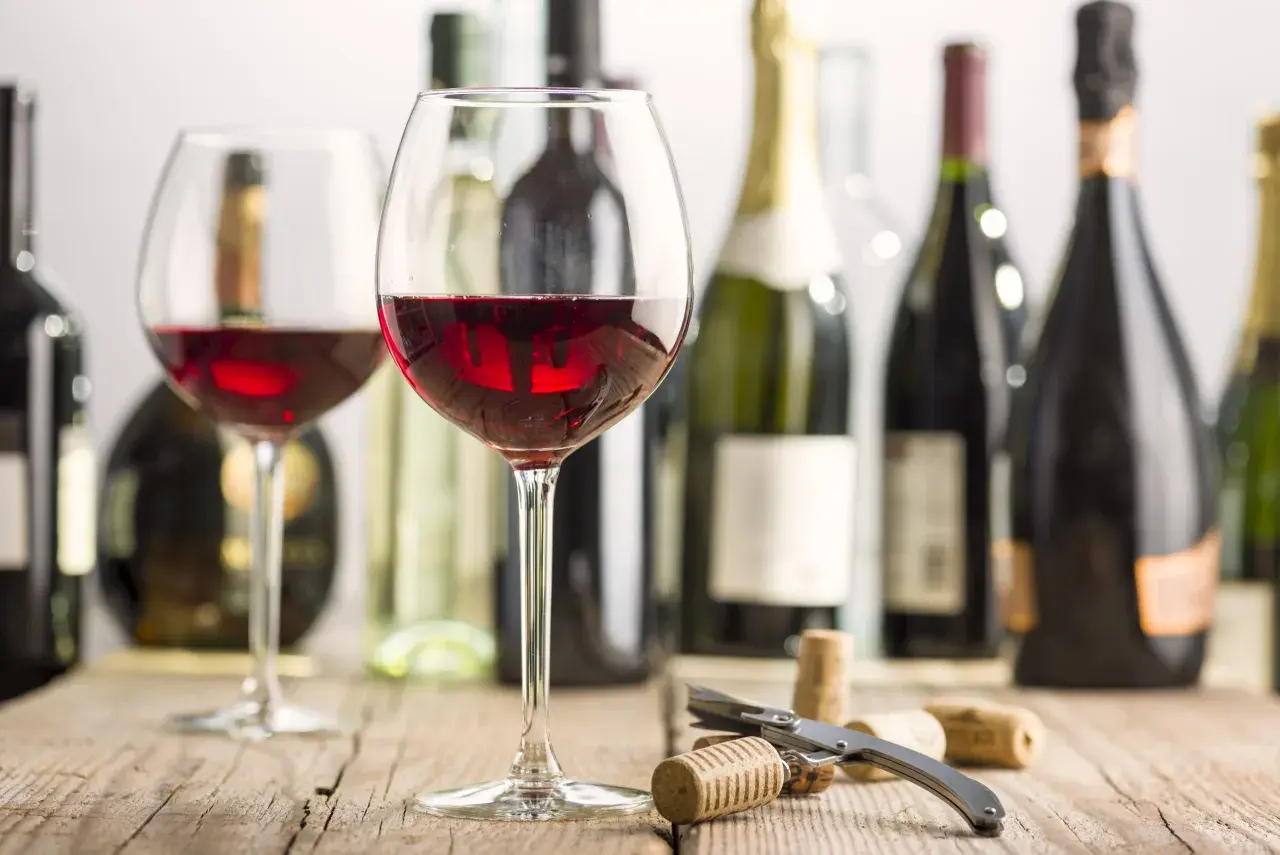 Two glasses of red wine, bottles, and corks on a wooden table. Imagine the rich, fruity mencia geschmack.