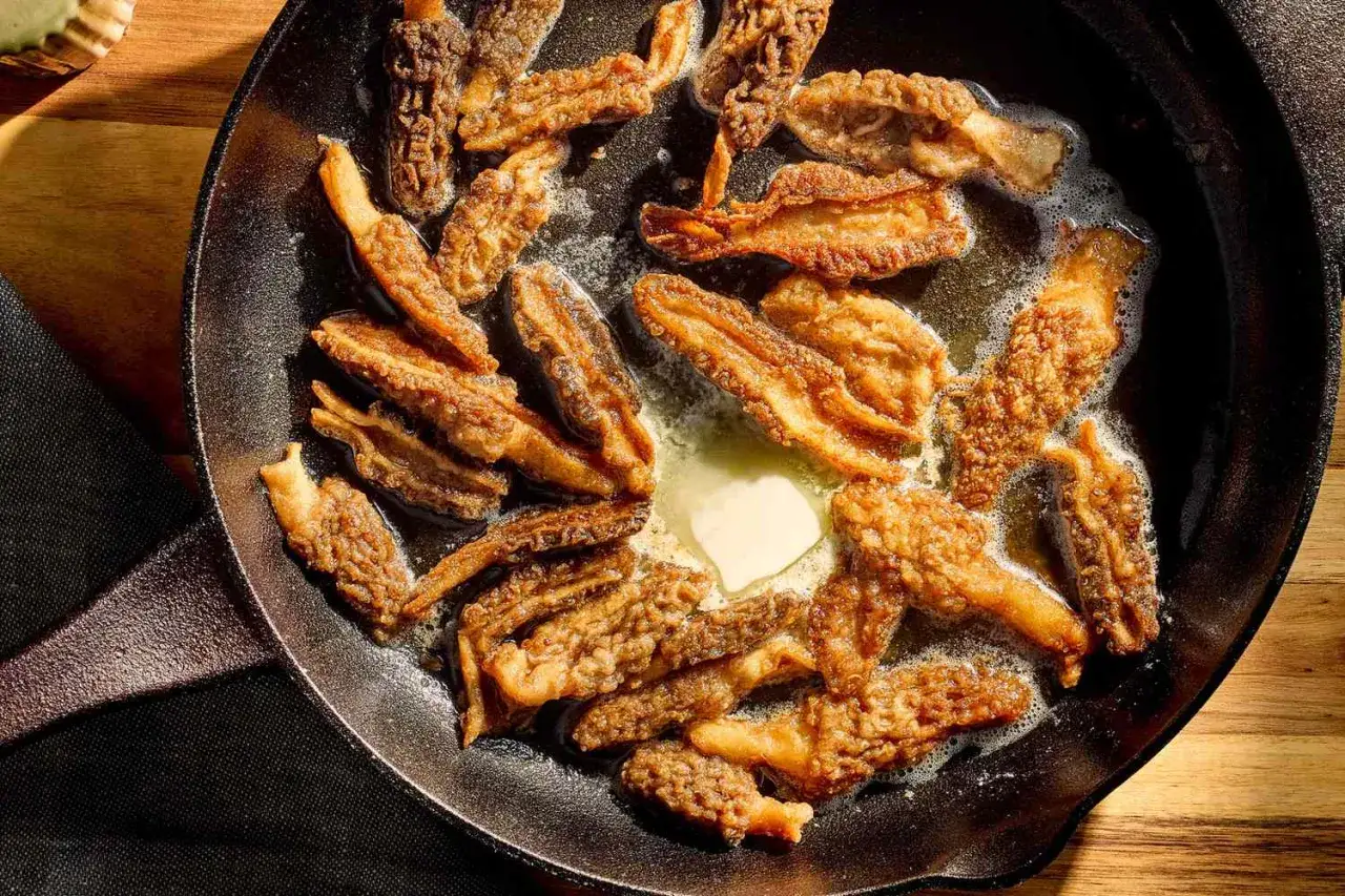 Golden brown fried morel mushrooms sizzle in a cast iron skillet with melting butter.