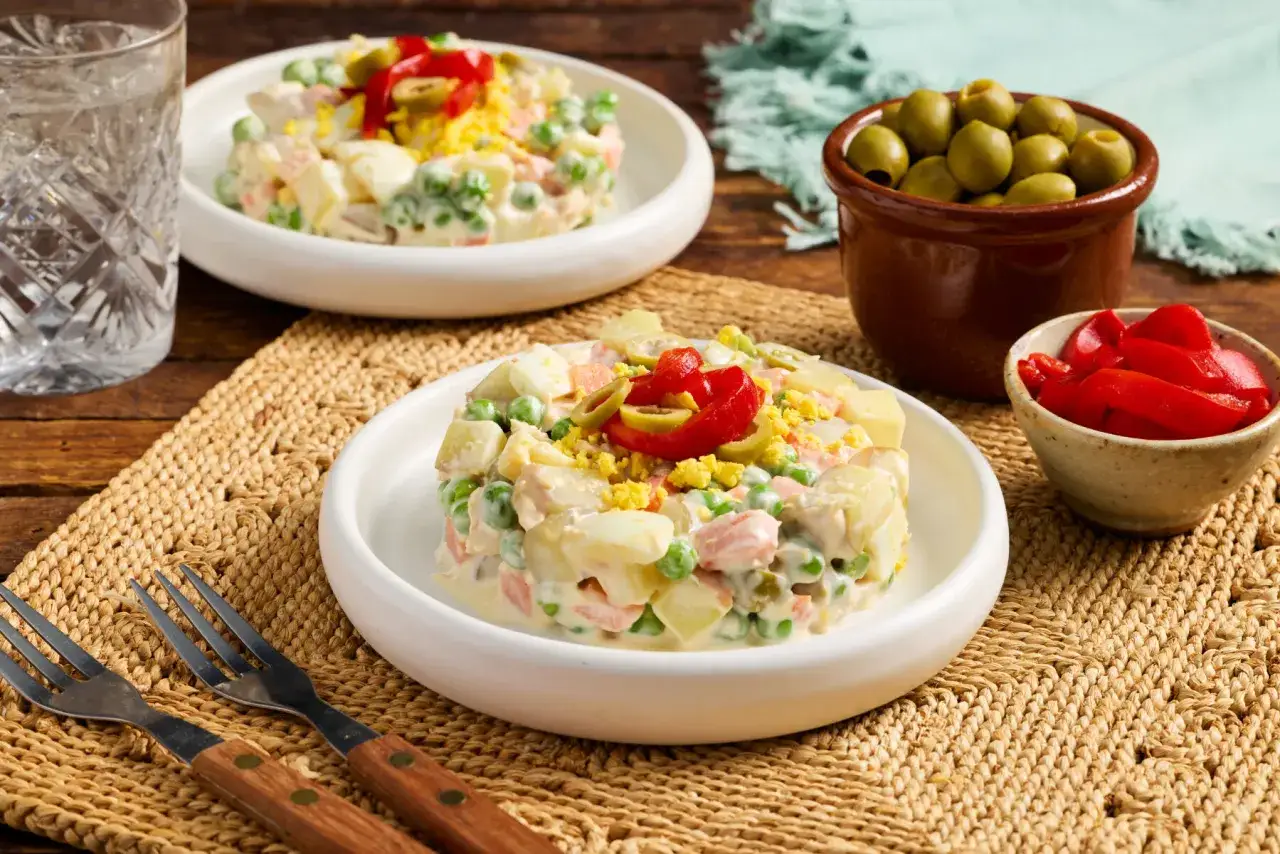 Two servings of ensalada rusa espa&ntilde;ola, a creamy potato salad with peas, carrots, and egg, garnished with olives and red pepper.