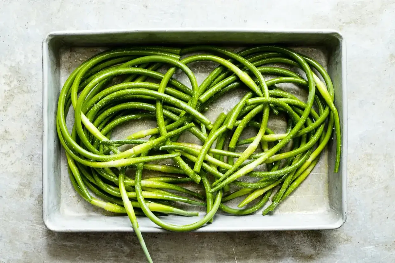 A baking tray filled with bright green, coiled garlic scapes, lightly seasoned and ready for roasting.