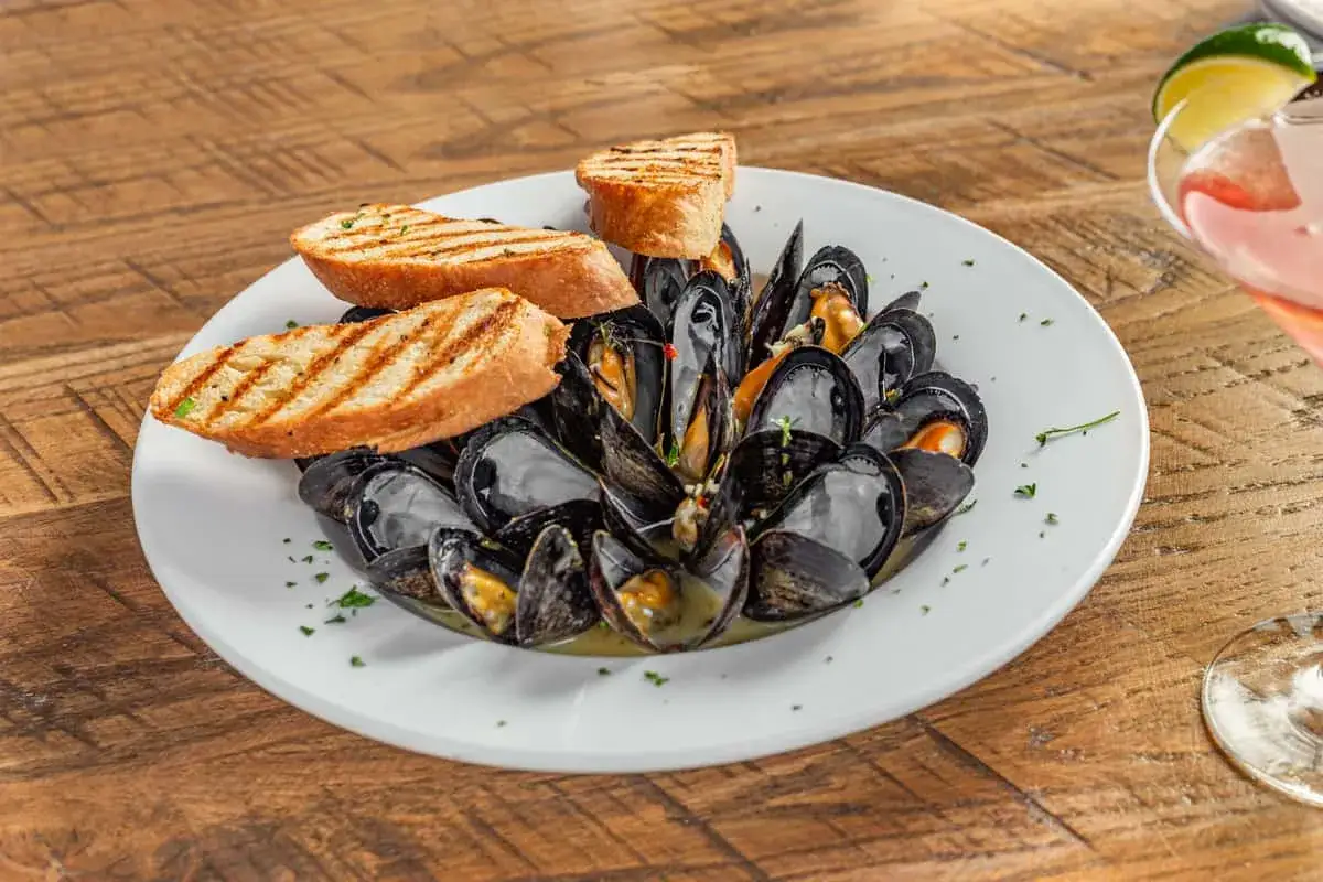A steaming plate of moules marini&egrave;re, brimming with dark mussels in a savory broth, is garnished with grilled bread slices.