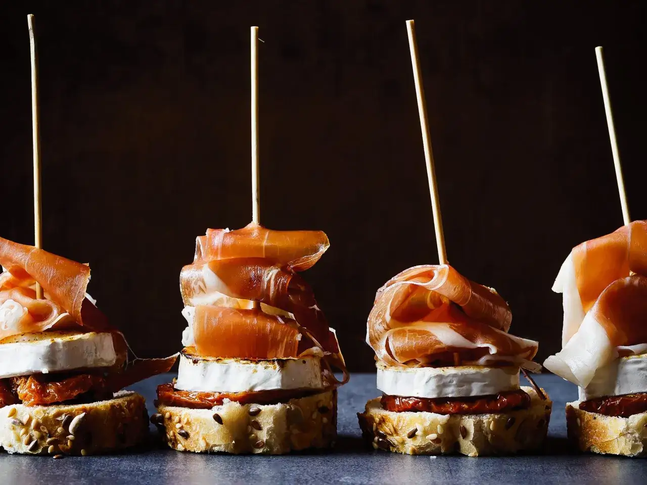 Gilda food skewers with prosciutto, goat cheese, and sun-dried tomatoes on seeded bread.