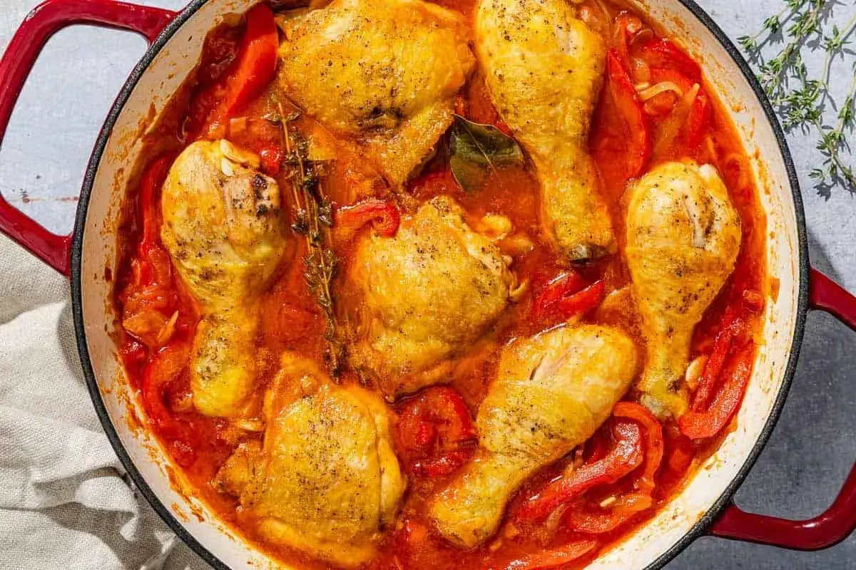 A rustic chicken basque dish, featuring golden-brown chicken pieces simmered in a rich tomato and pepper sauce with herbs.