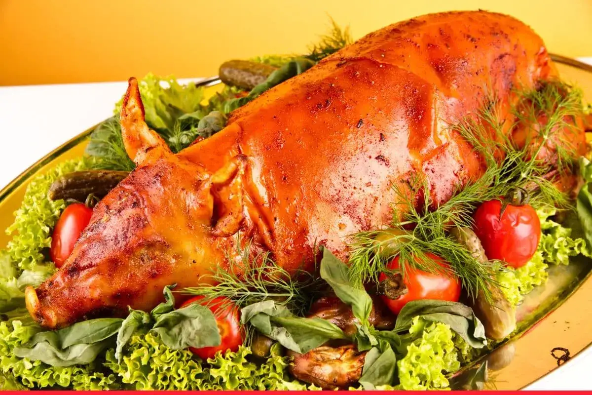 A golden-brown cochinillo asado, surrounded by fresh lettuce, cherry tomatoes, pickles, and dill, showcasing the perfect cochinillo asado ingredients.