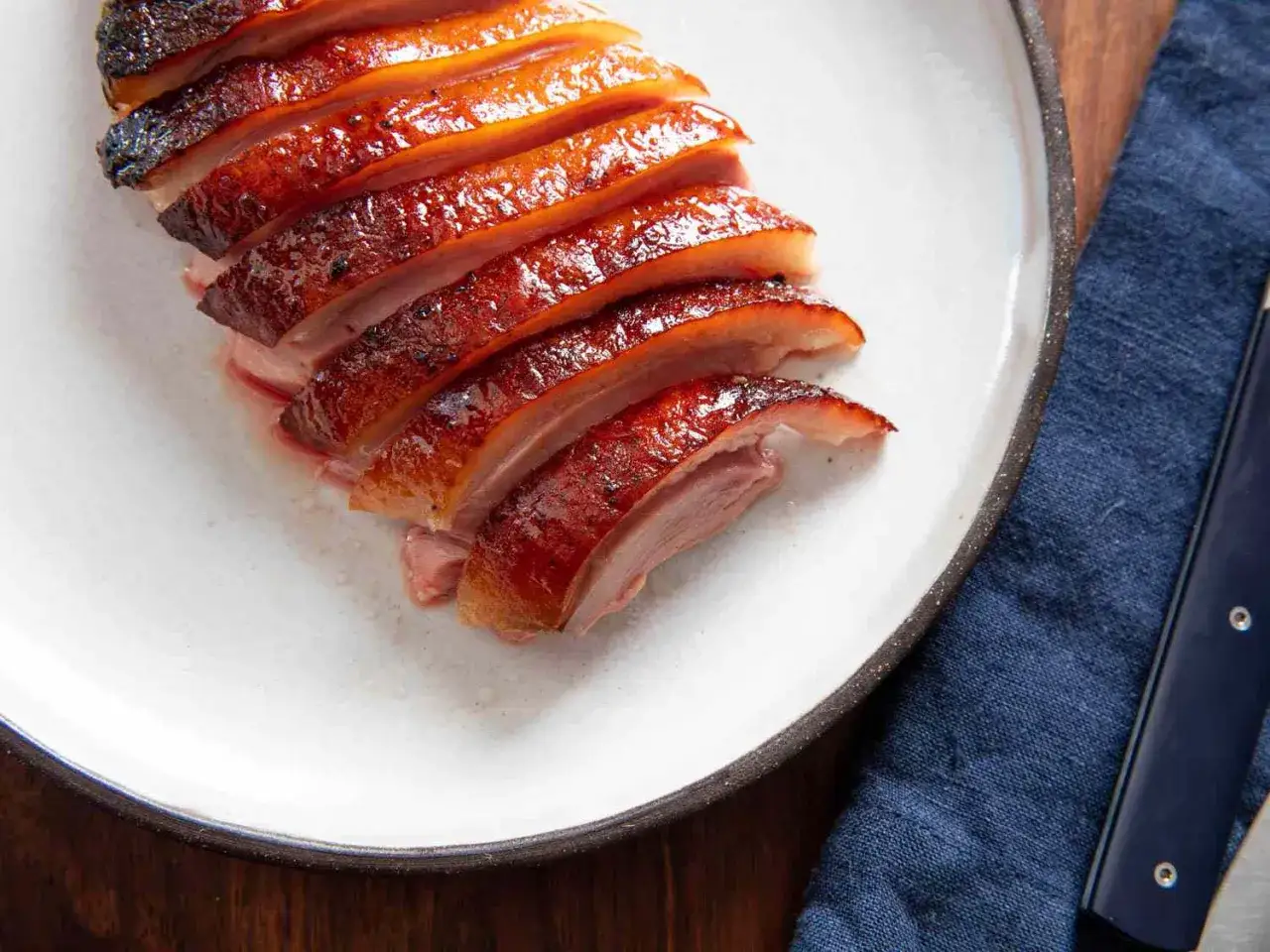 Crispy, glazed duck breast slices, a perfect duck breast recipe, served on a white plate with a dark blue napkin and knife.