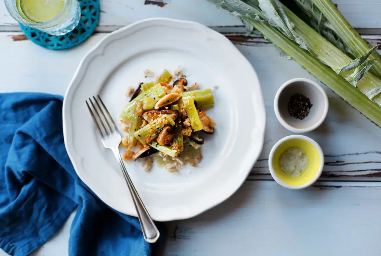 A delicious cardoon recipe with mushrooms and breadcrumbs, served on a white plate with a fork.