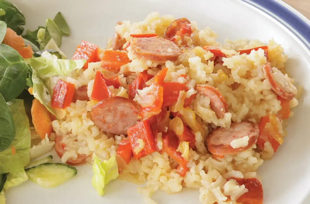 A delicious dish of how to cook roce, featuring rice with sliced sausage and red peppers, served with a side salad.