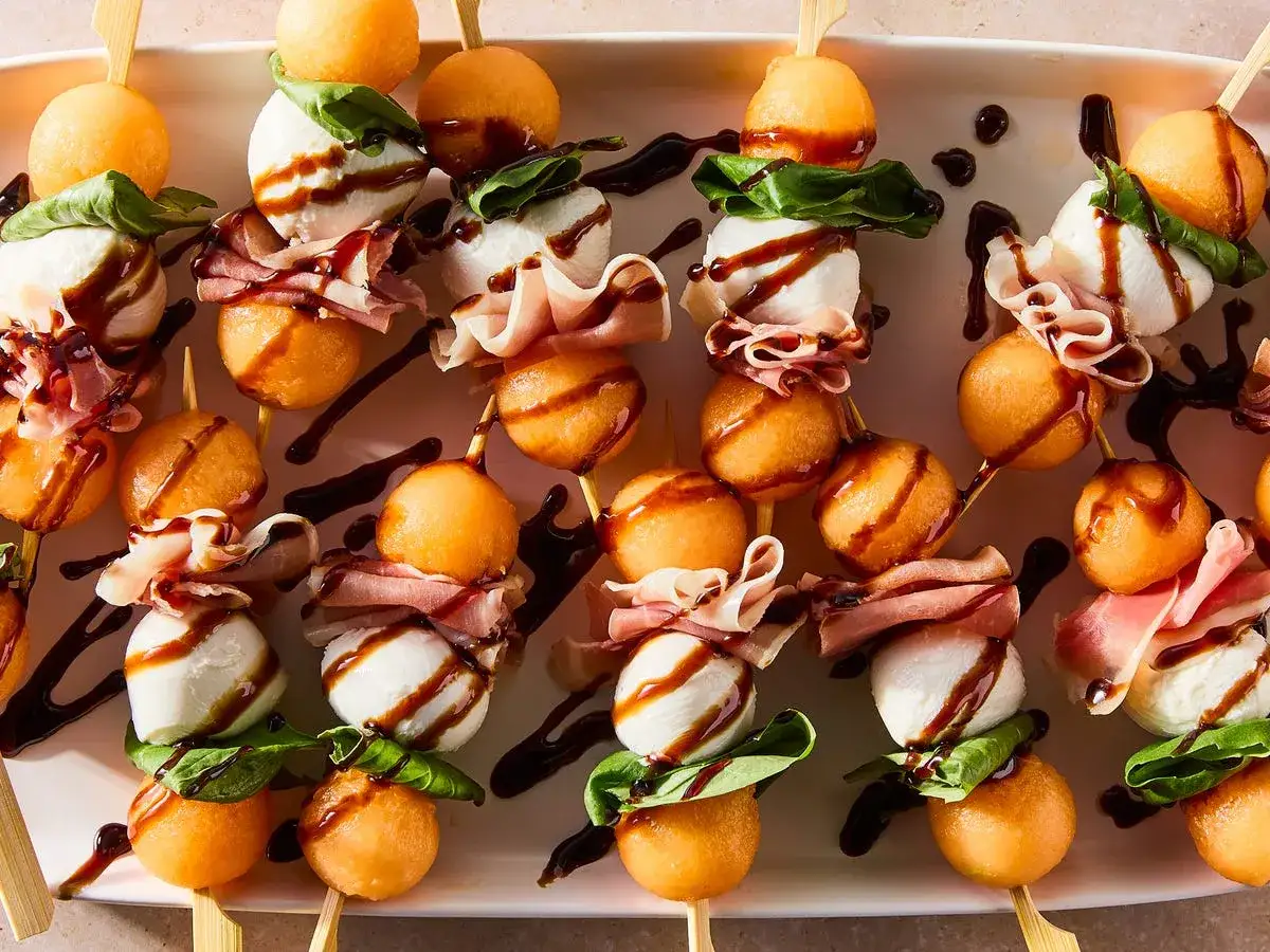 Melon con jamon skewers with mozzarella balls, basil, and balsamic glaze. A delightful appetizer!