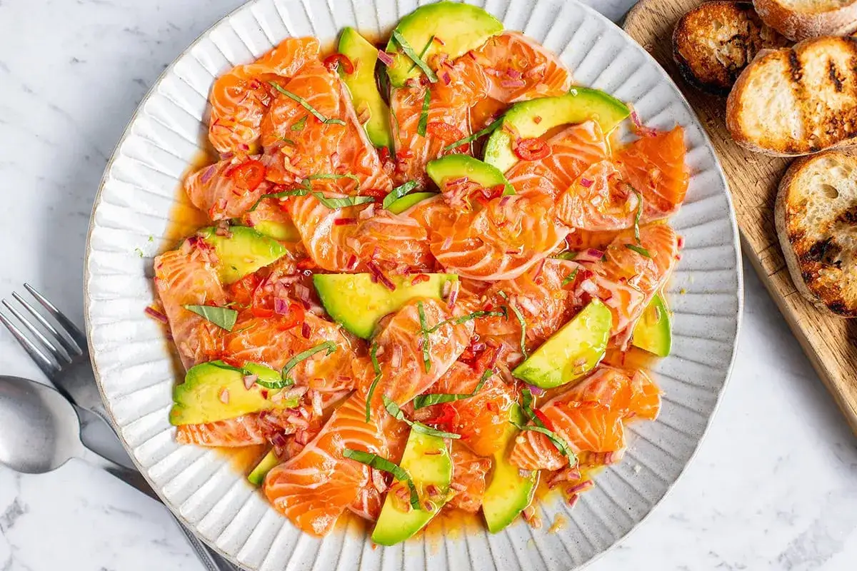 Vibrant salmon crudo with creamy avocado slices, red onion, and chili, drizzled in a bright dressing. A refreshing taste of what is salmon crudo.