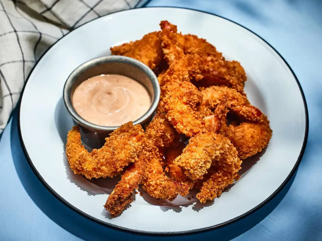 Crispy fried shrimp piled high on a plate, served with a creamy dipping sauce. A perfect appetizer for any seafood lover.