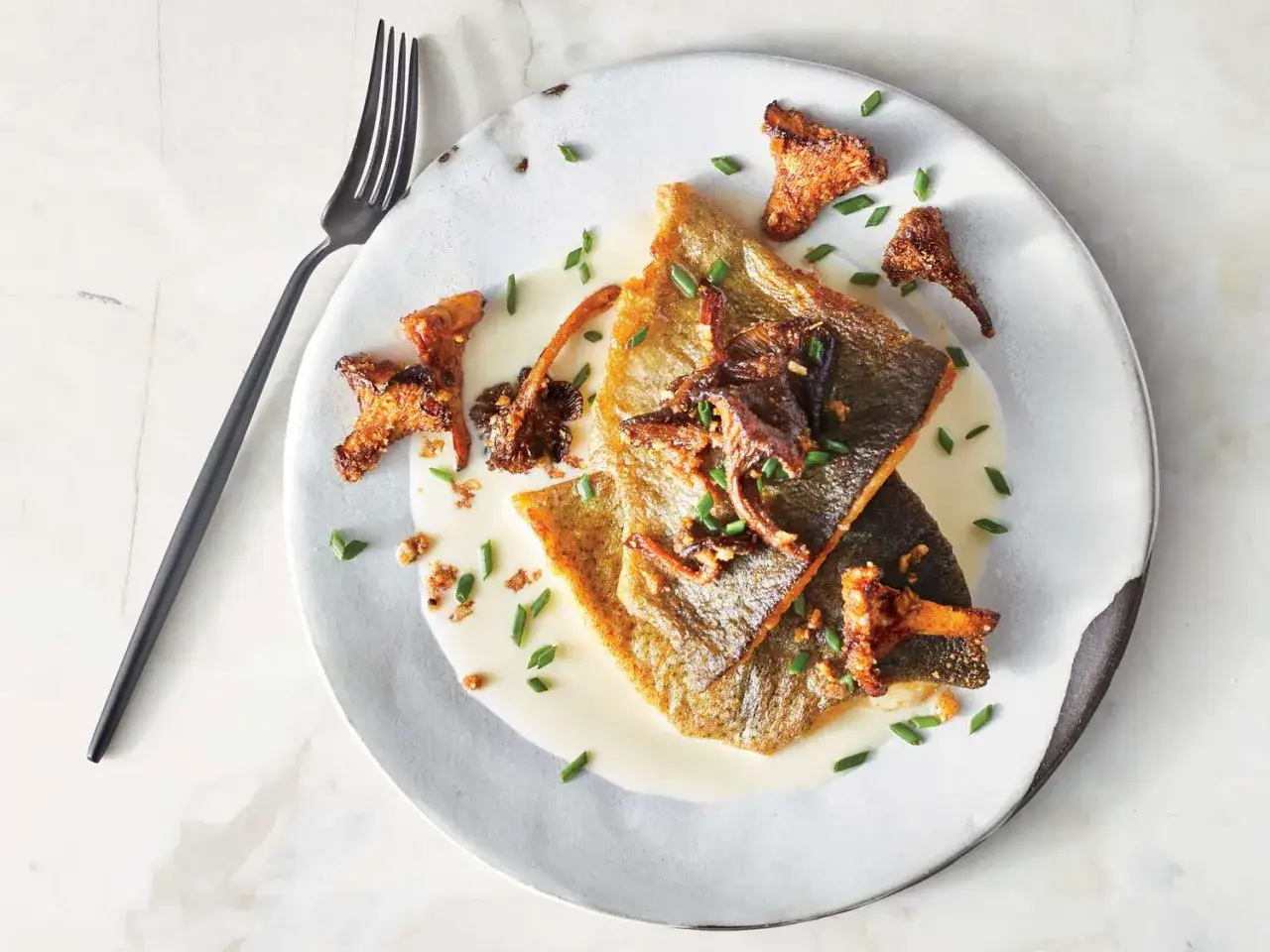 Pan-seared truchas fish fillets served with creamy sauce, chanterelle mushrooms, and chives. A fork rests to the side.
