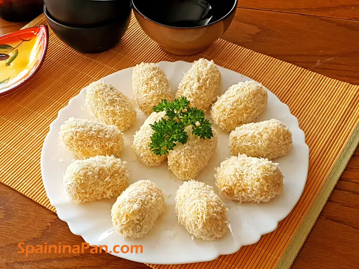 A plate of golden cod croquettes, coated in crispy breadcrumbs and garnished with parsley, ready to be enjoyed.
