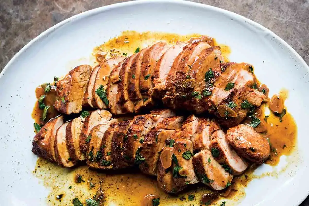 Juicy, sliced Spanish pork tenderloin glistening in a savory sauce, garnished with fresh herbs and garlic.