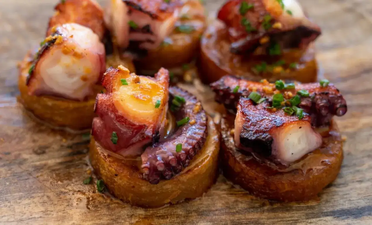 Delicious Spanish octopus dish, featuring tender grilled octopus pieces atop crispy potato rounds, garnished with chives and garlic.
