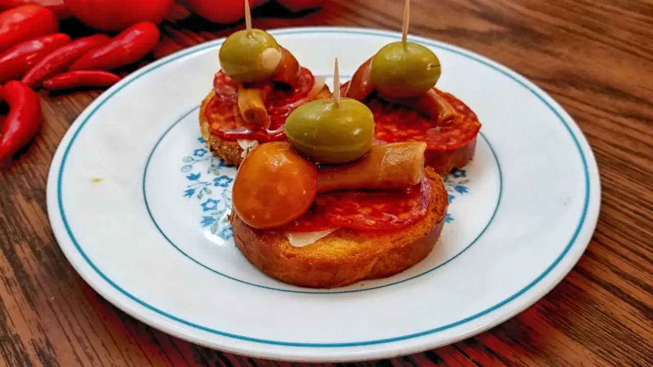 Three delicious chorizo tapas on a plate, topped with olives and cherry tomatoes.