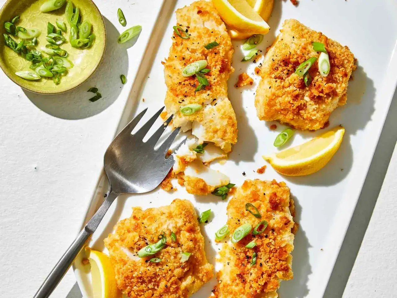 Crispy baked cod fillets, a simple way to cook cod, garnished with scallions and lemon wedges.