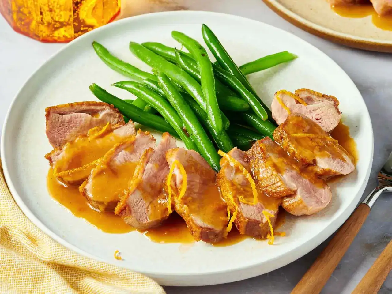 Slices of duck a l'orange, glistening with sauce and garnished with orange zest, served with bright green beans.