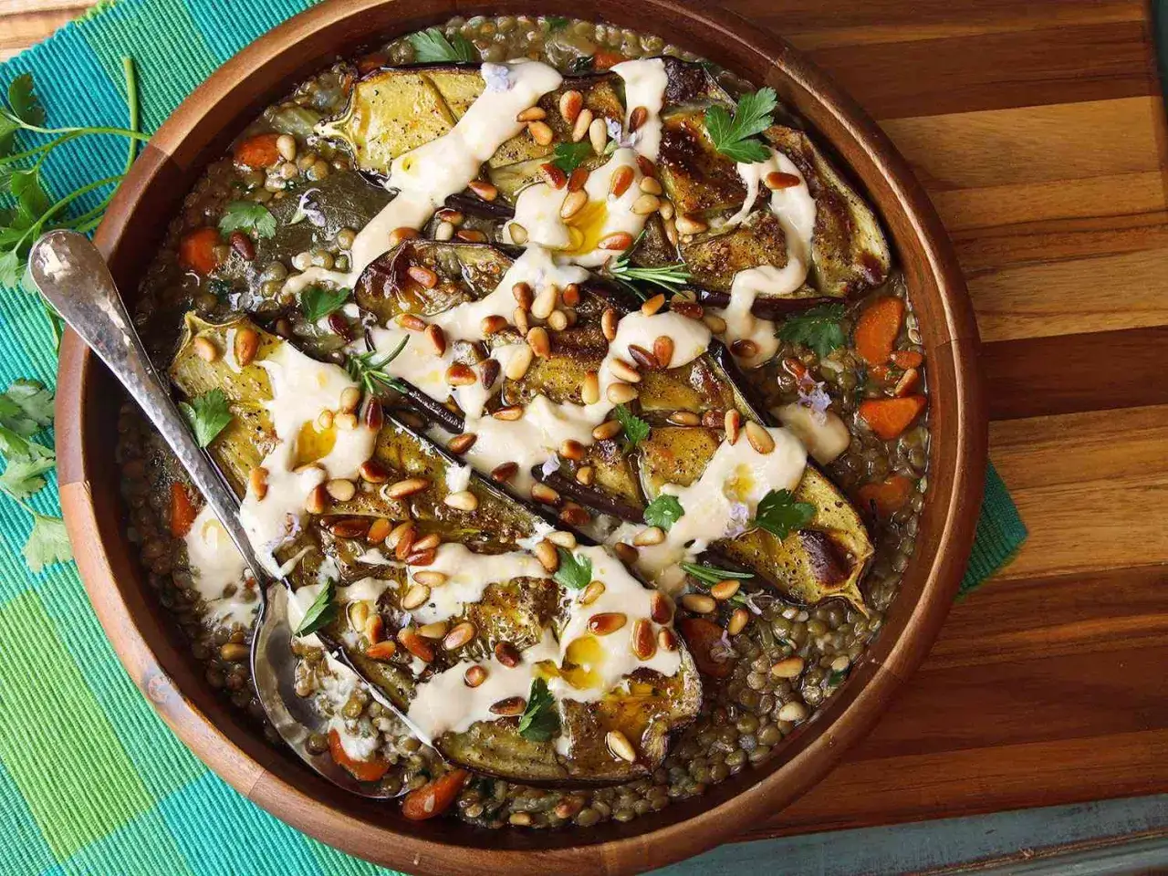 A delicious dish featuring roasted eggplant slices over a bed of lentils and carrots, drizzled with a creamy sauce and topped with pine nuts. A perfect example of creative eggplant recipes.